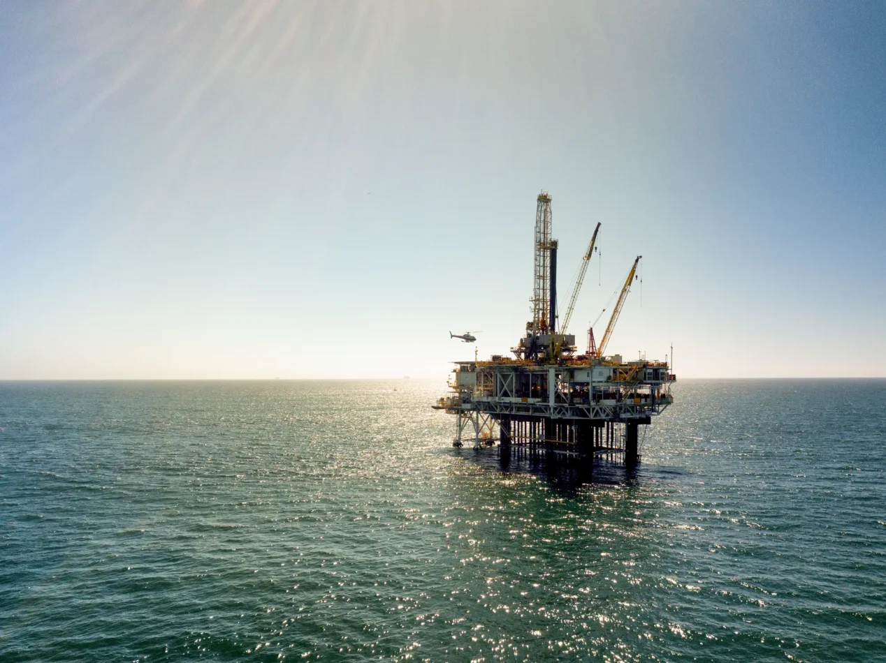 1. An oil rig stands prominently in the vast ocean, surrounded by water under a clear blue sky.